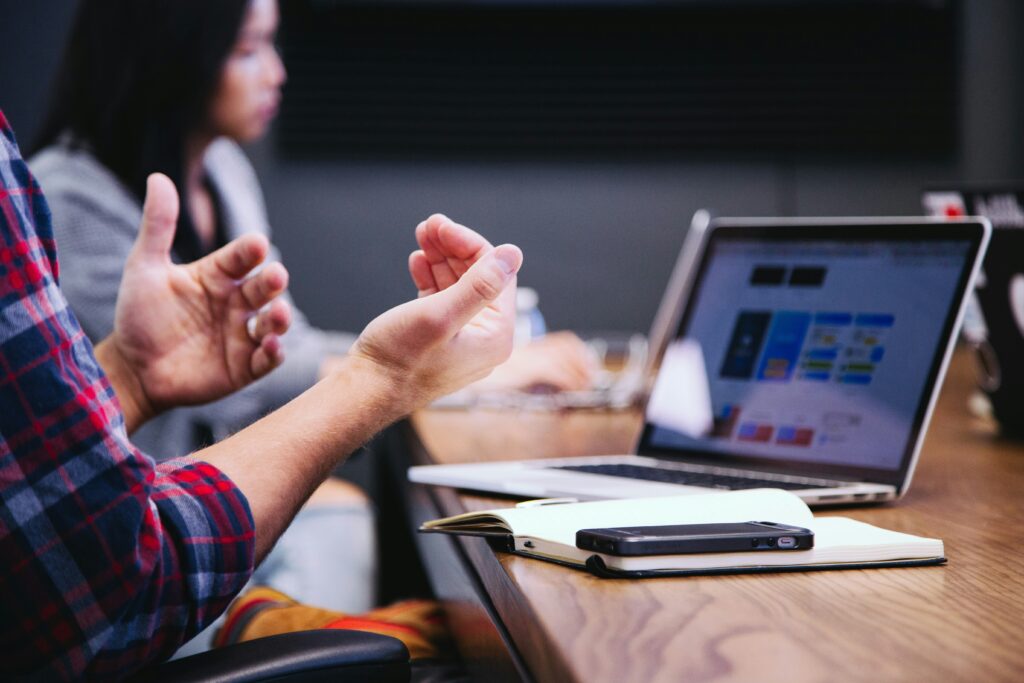 A person gesturing while on a video call at a table on a laptop.